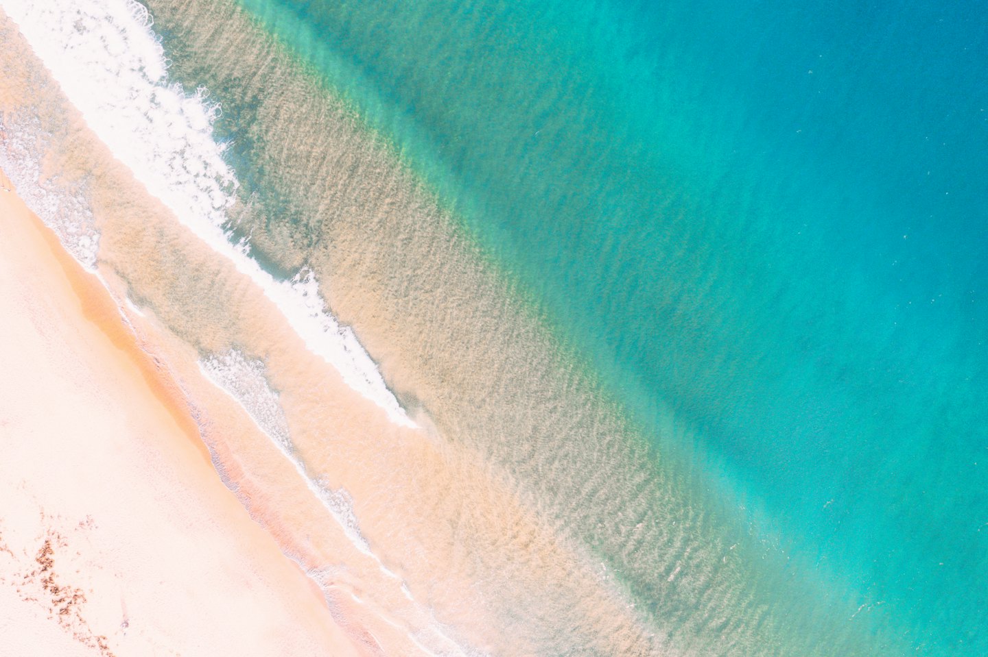 Vista aerea di acqua oceanica turchese che incontra una spiaggia sabbiosa.