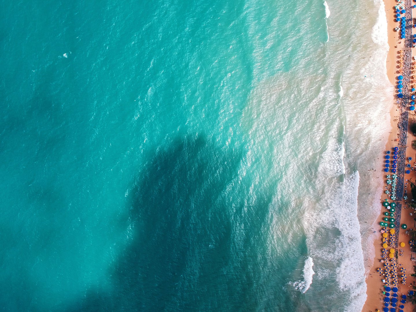 Acqua turchese dell'oceano incontra una spiaggia sabbiosa con ombrelloni colorati.